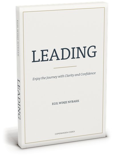 The LEADING paperback by Egil Winje Nybakk, standing at a slight angle: a cream cover with a thin brass frame, the navy title LEADING, the subtitle Enjoy the Journey with Clarity and Confidence, and the spine lettered in navy